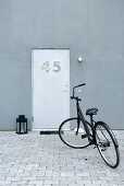 A black bicycle in a paved courtyard in front of a modern house with a unique front door