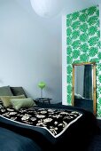 A large double bed with a floral quilt and an antique mirror in front of a a wall decorated with palm leaf patterned wallpaper