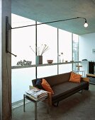 Wall lamp on swivelling cantilever arm and black leather couch in front of opaque glass wall in contemporary living space