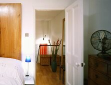 Bedroom with open door and view of stairwell with vase of flowers on parquet floor