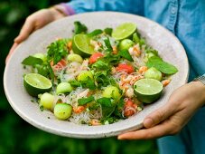 A woman holding a plate of glass noodle salad