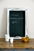 Blackboard with shopping list standing on rustic table leaning on wall