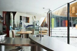 Offene Küche und Essplatz im Designerstil entlang gebogener Fensterfront mit Blick auf höher gelegenen Wohnraum-Ebene