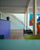 Kitchen counter, seating and modern art in clear, bold colours in living space with steel pillars and corrugated metal ceiling