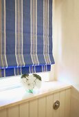Blue striped Roman blind and small posy above white-painted, wooden wall panel