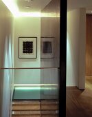 Blick von Glasbrüstung auf gerahmte Kunst und Glasboden am Treppenabsatz der offenen Holztreppe