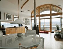 Dining table with modern, opaque glass top, director's chairs and retro lamp in open living space with arched ceiling