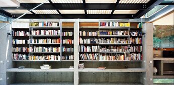 Two-storey concrete bookcase with sliding shelf units at front and gallery level in open steel and wood structure