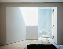 Schlafraum mit weißem Schalenstuhl im beleuchteten Vorraum vor dem Bad