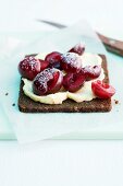 A slice pumpernickel topped with a spread and fresh cherries