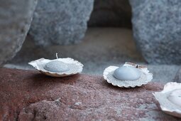 Zwei mit Sand und Schwimmkerzen gefüllte Muschelhälften auf einem Stein
