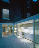 Courtyard with white tiled floor and view of illuminated kitchen in extension