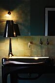 Detail of bathroom in half-light - table lamp with glossy lampshade on washstand with glossy surface