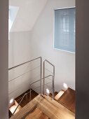 View of stairwell with modern wooden staircase and stainless steel balustrade