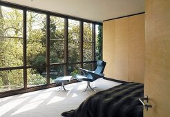 Schlafzimmer mit einem Sessel und Fussschemel vor der Fensterfront