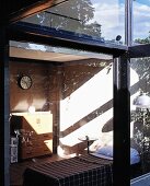 Blick durch Glasfassade mit breiten Schiebefenstern in sonnigen Schlafraum mit unverputzten Wänden