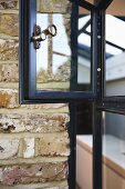 Old brick wall and historic, metal-framed window with brass latch on open casement