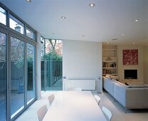 Open-plan, modern room with sofas and dining area in front of wide glass wall