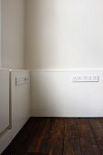 Half-height, white wood panelling with rows of plug sockets above old floorboards
