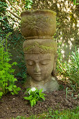 Buddha-Kopf aus Stein mit integriertem Pflanzengefäss in Gartenbeet