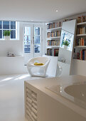 A modern plastic chair in front of a shelf of books in a bedroom with part of the bath, featuring a built-in shelf, in the foreground