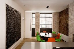 Open-plan room with dining area and colourful shell chairs next to brick wall