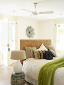 Table lamp on barrel-shaped cabinet next to bed with headboard and various scatter cushions in modern bedroom