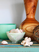 Seashells in dish in front of wooden vase on shelf