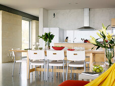 Dining table made of light wood with white plastic chairs in an open kitchen