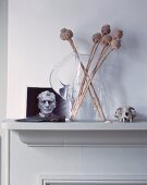 Dried poppy heads in glass jug next to photograph on mantelpiece