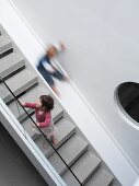 Unconventional staircase design with bulls-eye window and slide alongside classic modern stairs with glass balustrade