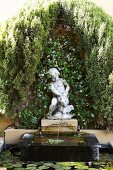 Ornamental fountain with stone figure in front of facade covered with climbers