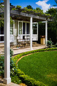 Pergola with climbers above terrace adjoining house in manicured garden