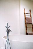 Frei stehende Badewanne mit Standarmatur und eine Leiter als Handtuchhalter in einem Badezimmer