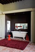 Bordeaux-red rug in front of free-standing vintage bathtub in niche painted dark grey