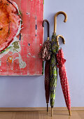 Colourful detail of three walking-stick umbrellas leaning on lavender blue wall next to contemporary painting in hallway