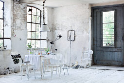 Table with tablecloth and various white chairs in dilapidated room in former factory