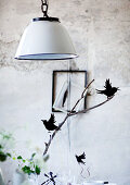 Pendant lamp with white metal lampshade above bird ornaments on twig