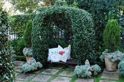 Arch lushly overgrown with climbers and old iron bench with romantic scatter cushions in French terrace garden