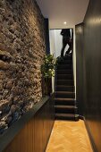 Beleuchtete Natursteinwand in schmalem Treppenhaus