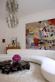 Geschwungene, weiße Wohnzimmercouch mit zerklüftetem Couchtisch aus lackierter Teakwurzel; im Hintergrund ein modernes Gemälde