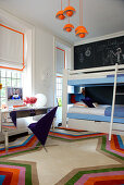 Bunk beds in children's bedroom with bright orange accents and one wall painted with black chalkboard paint