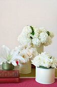 Various white flowers in white tins and two old books on striped tablecloth