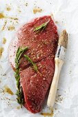 Raw Steak in a Rosemary Marinade on Butcher's Paper; Basting Brush