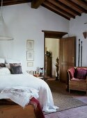 Bed with white bedspread and wicker chair in simple bedroom with open door