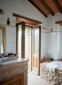 Brick-built washstand and bathtub in modernised bathroom with open terrace door