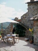 Mediterraner Terrassenplatz mit Sonnenschirm vor alten Natursteingemäuern