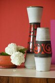 Set of 70s-style vases and white carnations in bowl against red-painted wall