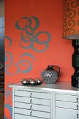 Chest of drawers painted light grey against red wall with retro-style circular pattern