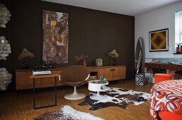 Cow skin rug next to shell chair at desk and dark brown wall in 70s-style room
